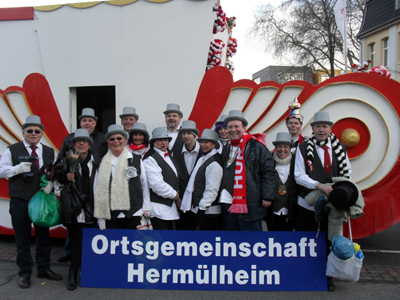 Einen pr&auml;chtigen Zug durfte Herm&uuml;lheim dieses Jahr bewundern. Organisiert von Sascha Baumhardt als Zugleiter der Ortsgemeinschaft Herm&uuml;lheim unter dem Vorsitzenden Oliver Franz wird der Karneval in Herm&uuml;lheim jedes Jahr besser. P&uuml;nktlich beim Abmarsch in der Sudetenstrasse &ouml;ffnete sich der wolkenverhangene Himmel und wir wurden von einer strahlenden Sonne begr&uuml;&szlig;t. Mehr Teilnehmer, darunter neu eine sehr gro&szlig;e Gruppe der Deutschherrenschule und einer sehr sch&ouml;nen Gruppe der Caritas schm&uuml;ckten unseren Zog. Und so sind wir angesichts der durchaus positiven bis begeisterten Reaktion der Bev&ouml;lkerung auch nach Abschluss bester Laune vor dem Wagen der Ortsgemeinschaft. V. li. n.re: Willy Harff, Sascha Baumhardt, Despina Vassou, Ria, Christa, Oliver Franz, Ruth Braun, Harald, Roman, Anne Quack, Ina Metternich, David Boventer, Panagiota Boventer, Josef Dohmen, Bernd R&auml;cke.